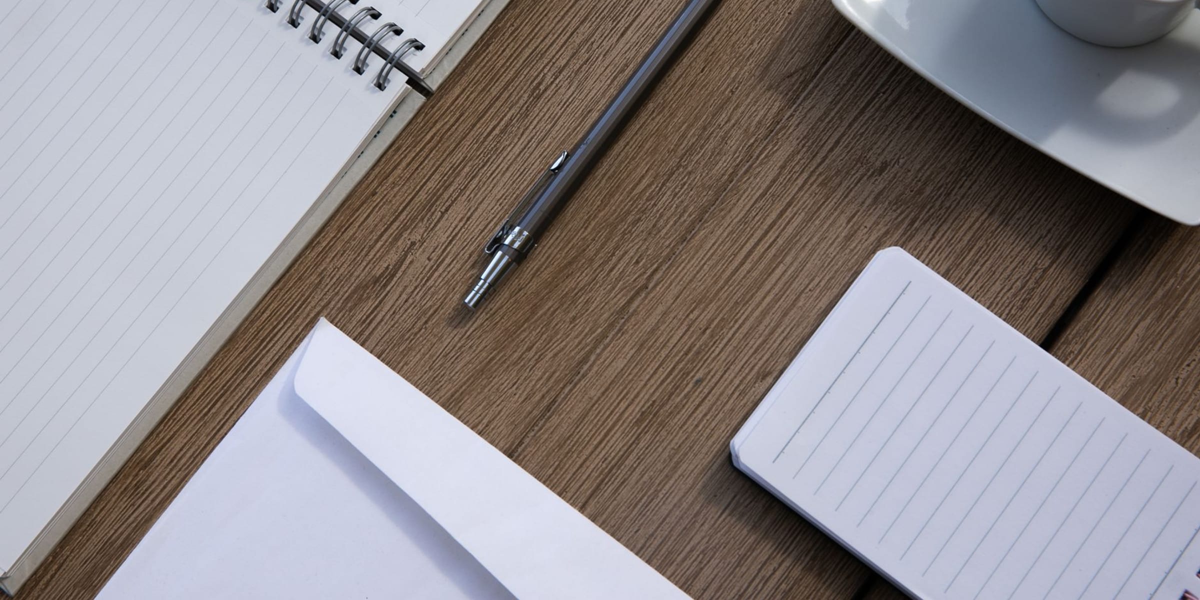 A calm, tidy desk with a notebook, pen, and coffee mug in soft morning light